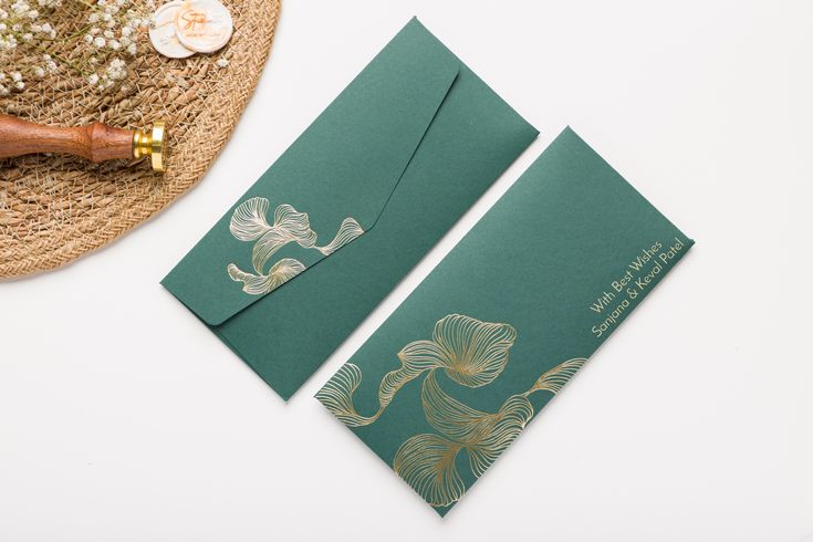 two green envelopes sitting on top of a table next to a straw hat and flower