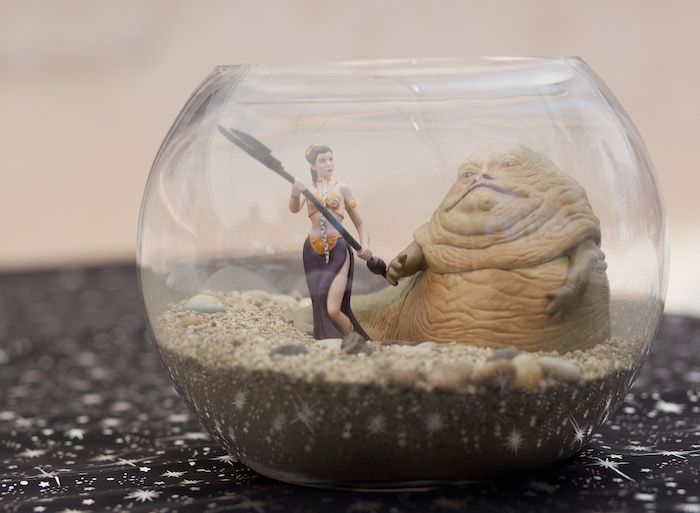 a star wars action figure is in a glass bowl with sand and gravel around it