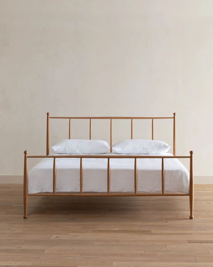 a metal bed frame with white sheets and pillows on top of it in a room