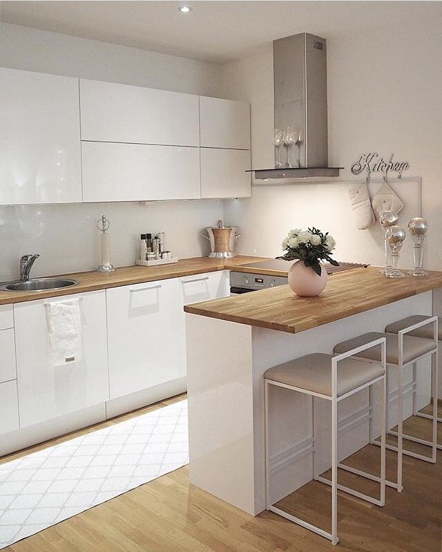 a white kitchen with wooden counter tops and stools in front of the stove top