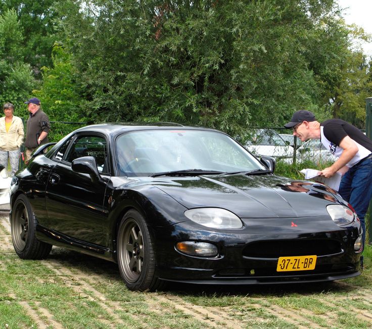 two men looking at a black sports car in the grass with other people around it