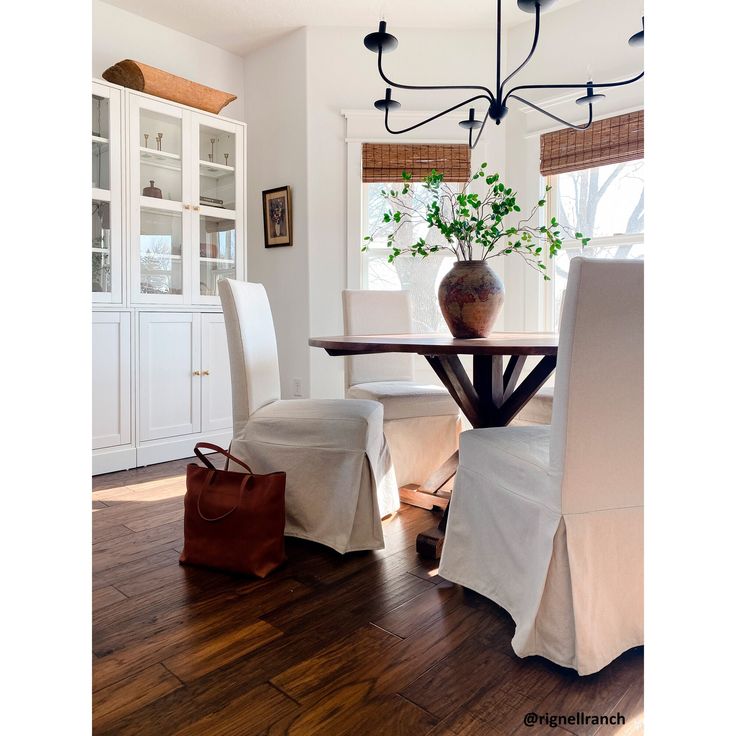 a dining room table with white chairs and a vase on top of the table in front of it