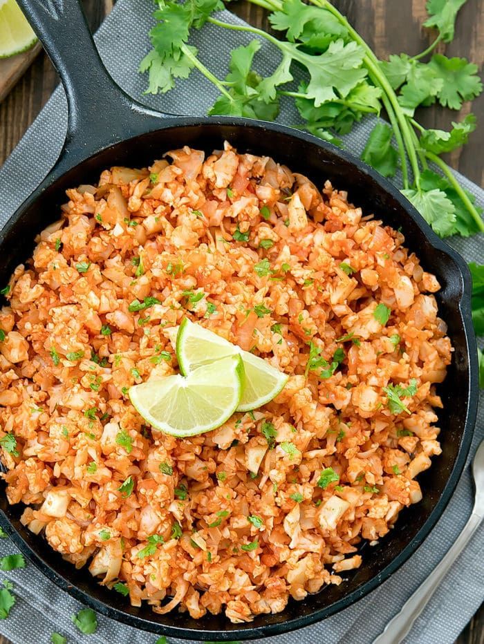 mexican rice in a skillet with cilantro and limes on the side