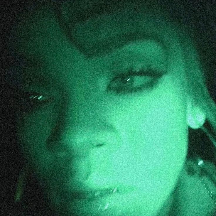 a close up of a person with green light on her face and hair in the dark