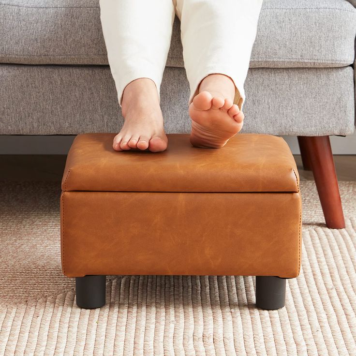 a person sitting on top of a foot stool in front of a couch with their feet propped up