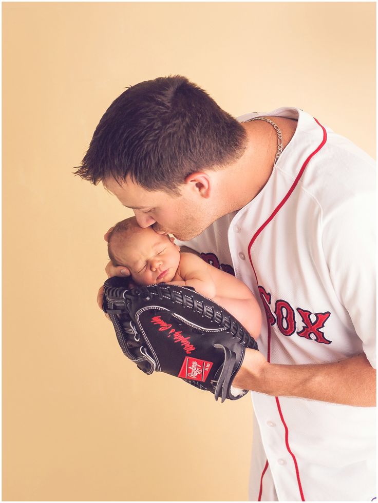 a man holding a baby in his baseball mitt and kissing it's face