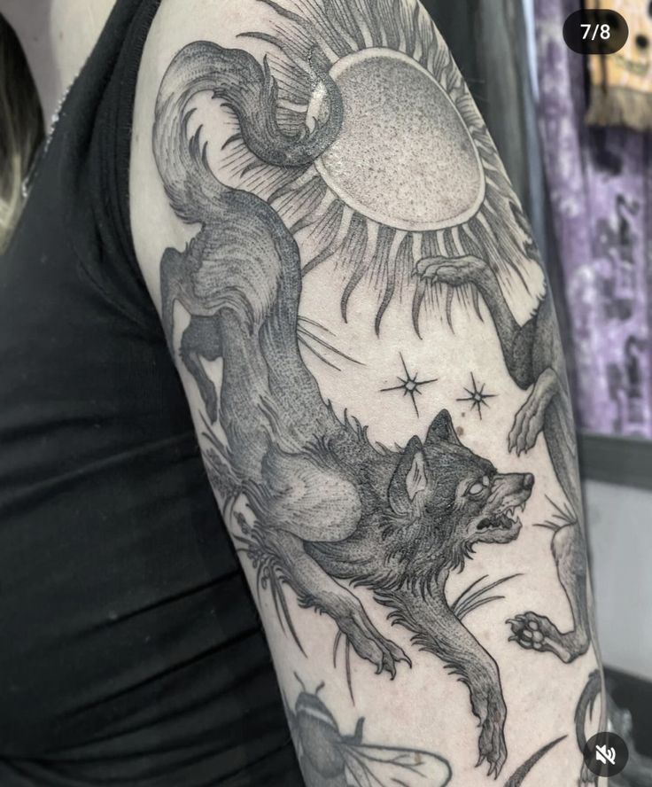 a woman's arm with a wolf and sun tattoo on the back of her shoulder