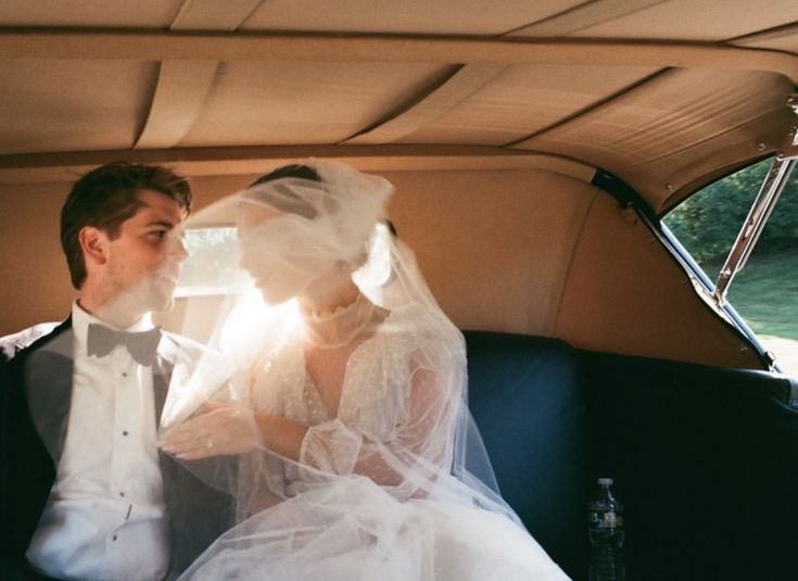 a bride and groom sitting in the back of a car