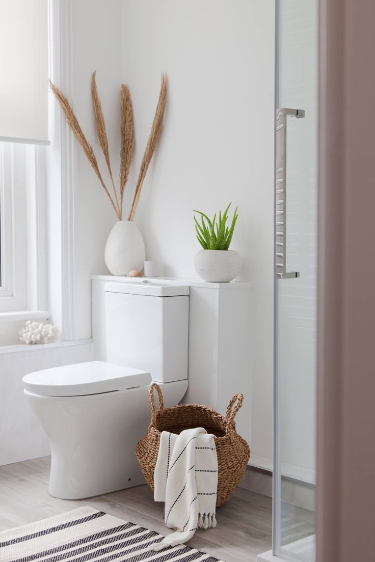 a white toilet sitting next to a bath tub in a bathroom under a window with plants on top of it