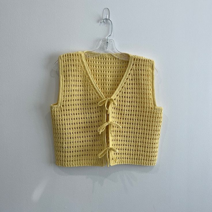 a yellow knitted vest hanging on a white wall