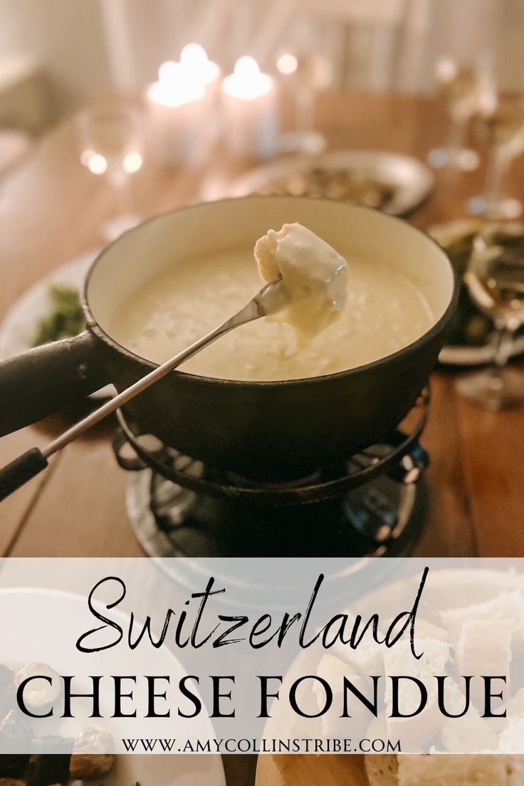 a bowl of cheese fondue on a table with bread and wine glasses in the background