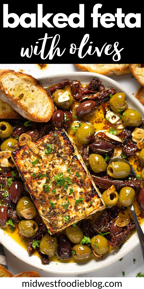 baked feta with olives on a white platter surrounded by toasted bread