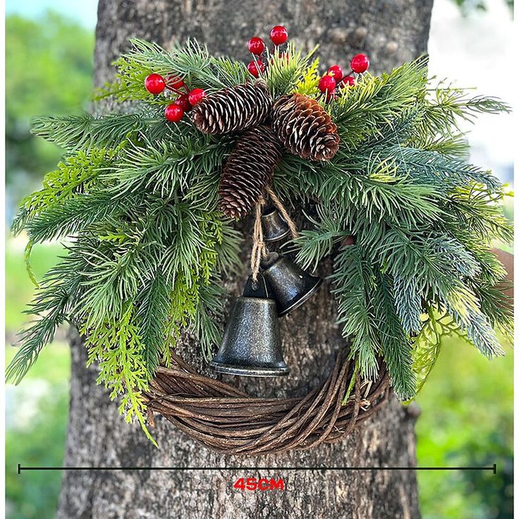 a christmas wreath with bells hanging from the side of a tree, surrounded by pine cones and red berries