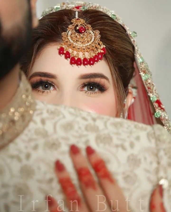 the bride is holding her veil over her face and looking at the groom's reflection