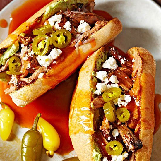 two hot dogs with toppings sit on a plate next to pickles and jalapenos