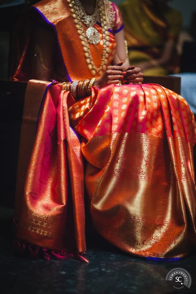 a woman sitting on top of a chair wearing a red and gold sari dress