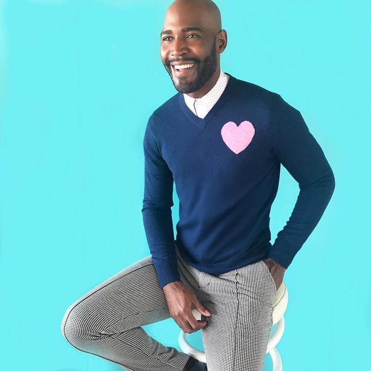 a man in a blue sweater with a pink heart on his chest posing for the camera