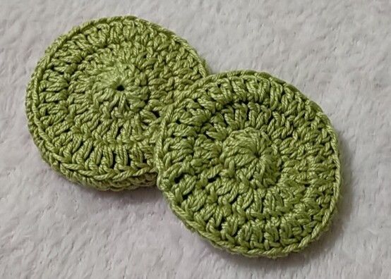 two green crocheted coasters sitting on top of a white cloth covered floor