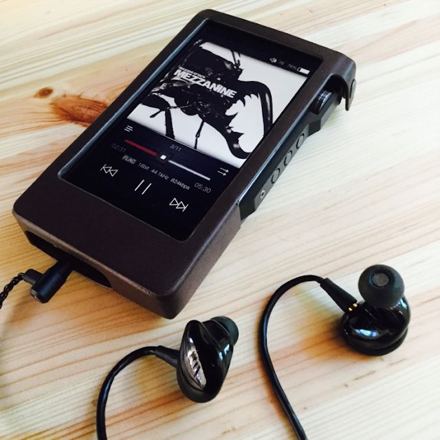 an mp3 player sitting on top of a wooden table next to ear buds and headphones