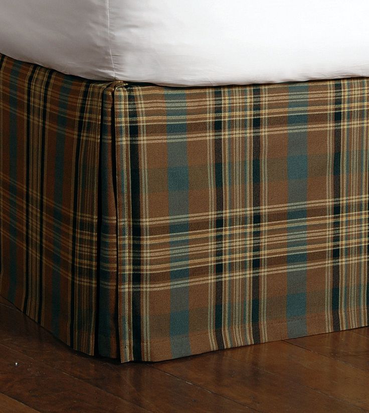 a bed with a plaid bedskirt on top of it and a white pillow