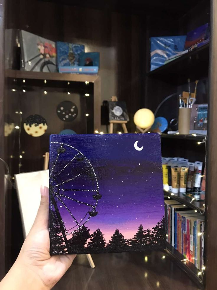 a hand holding up a card with a ferris wheel in the sky and trees on it