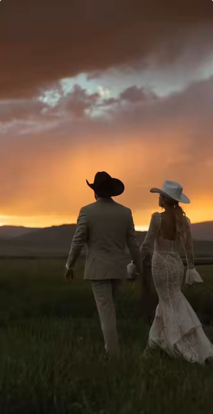 a man and woman walking through a field at sunset