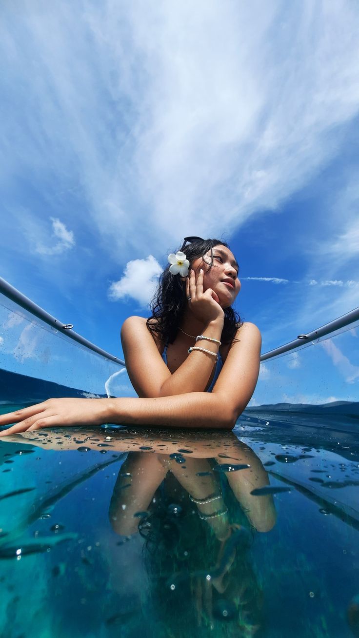 a woman sitting in the water talking on her cell phone while looking up at the sky