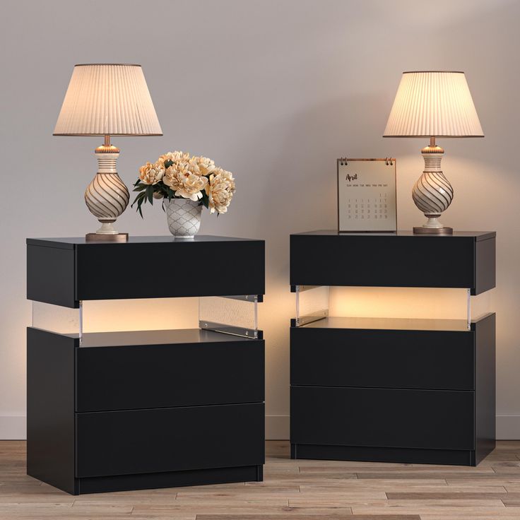 two black night stands with flowers on top and one lamp on the side next to each other