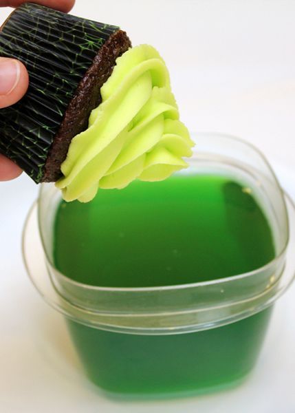 a hand holding a brush over a green substance in a plastic container on a white surface