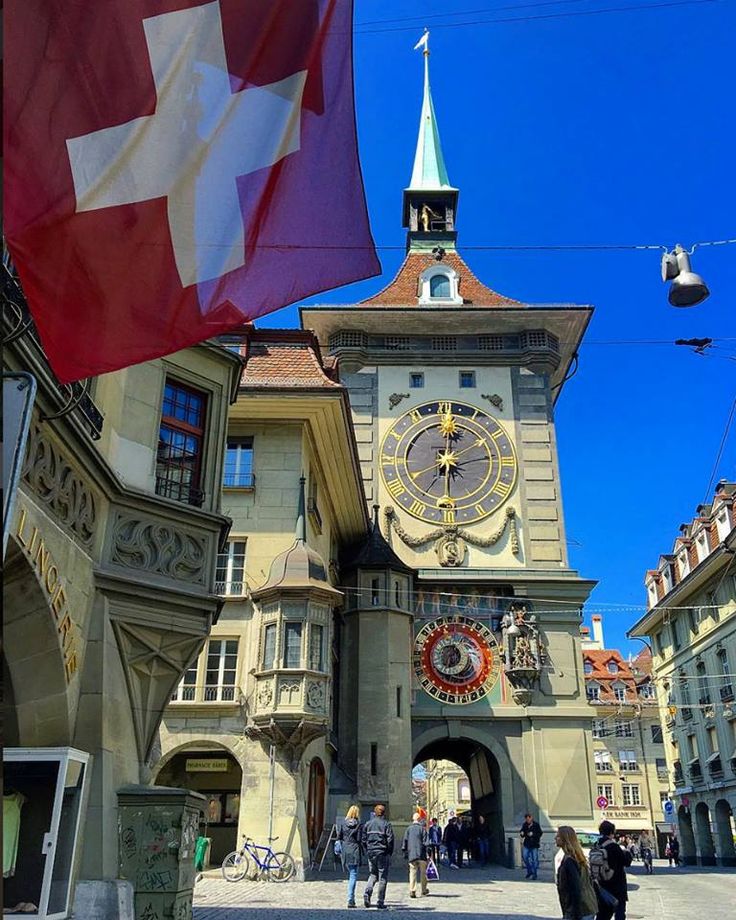 a large building with a clock on it's side and people walking around in front