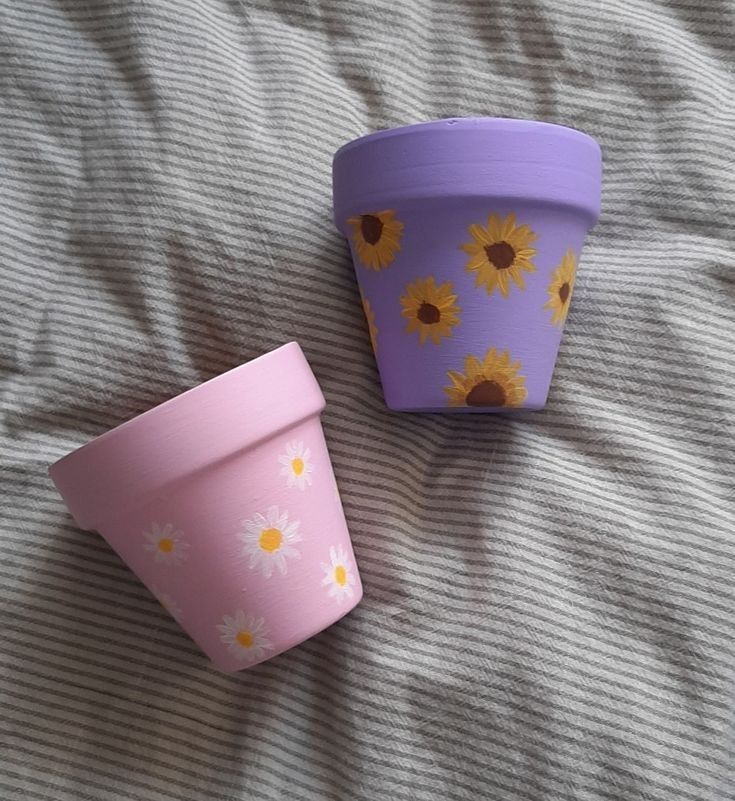 two flower pots sitting on top of a bed next to each other with yellow flowers painted on them