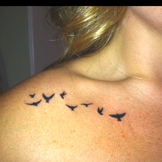 a woman's back shoulder with birds flying in the sky on her left side