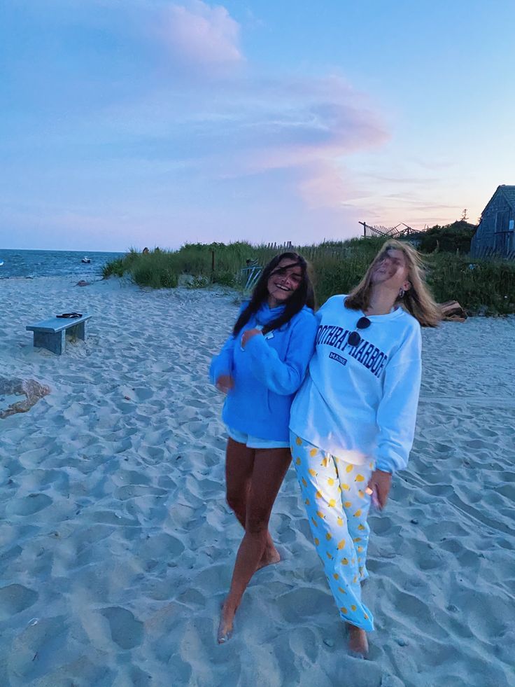 two women are standing on the beach at sunset with their arms around each other and smiling