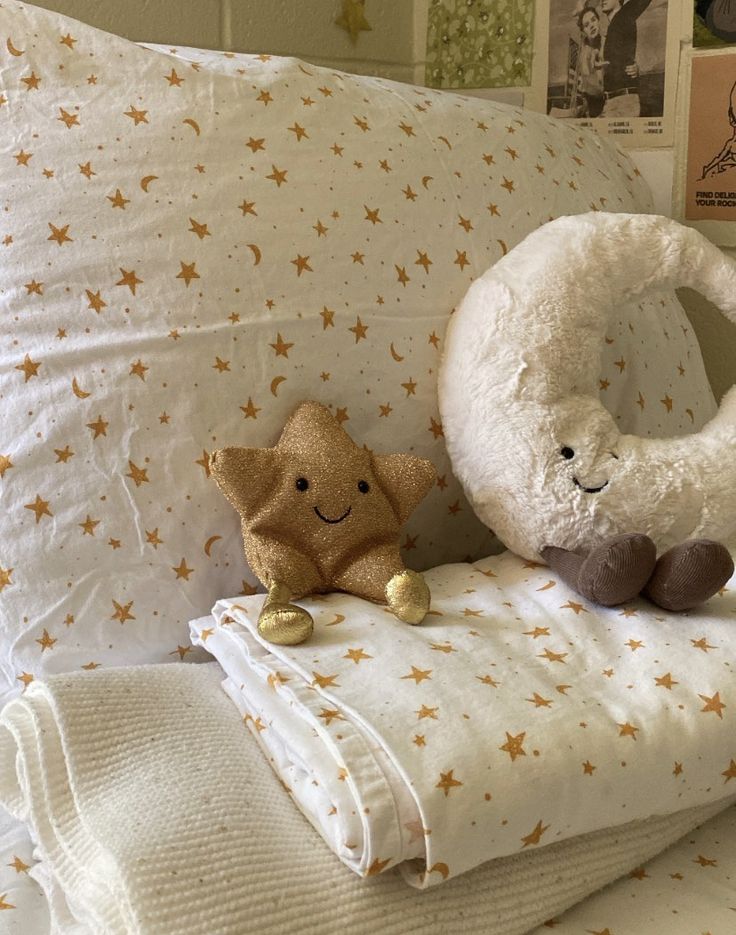 two stuffed animals sitting on top of pillows in a bed with white sheets and gold stars