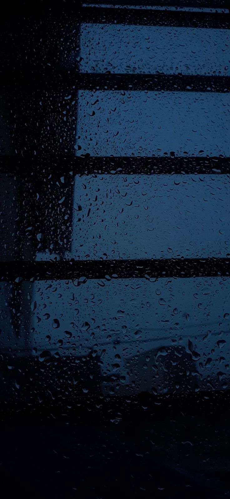 rain drops on the window as it is dark and drizzled with blue light