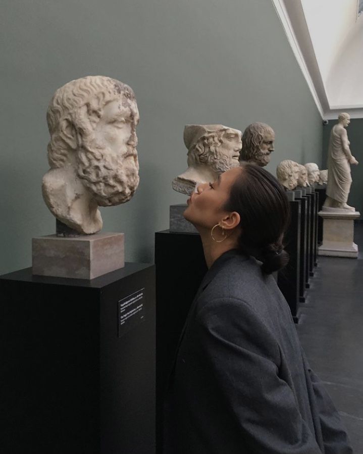 a woman looking at some statues in a museum