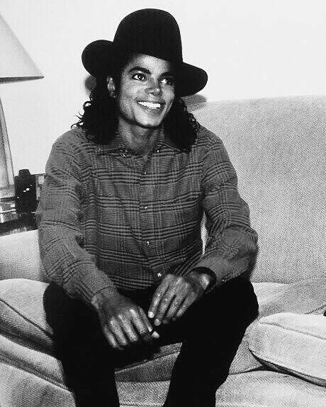 a black and white photo of a person sitting on a couch with a hat on