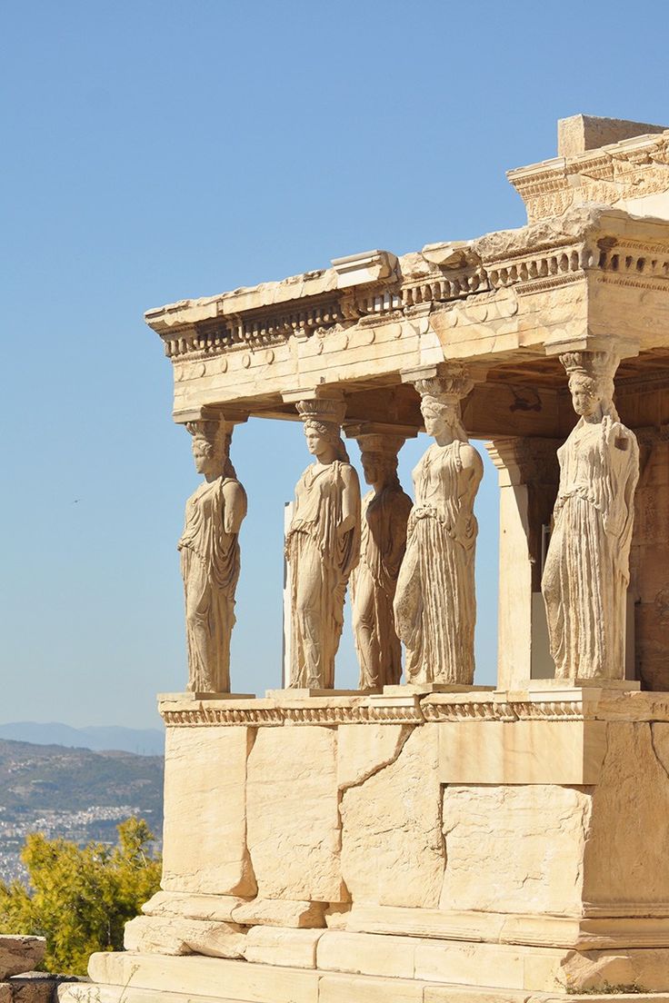 some statues on the side of a building with mountains in the background and blue sky