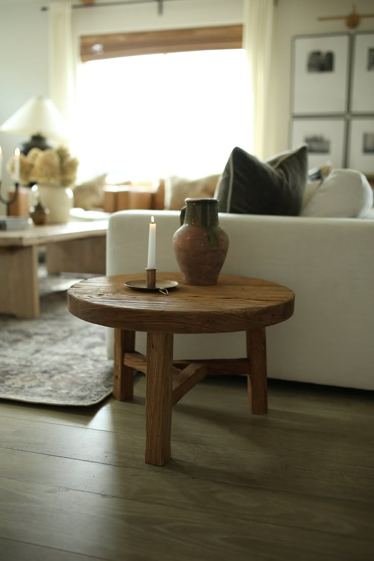 a table with a candle on it in front of a white couch and coffee table