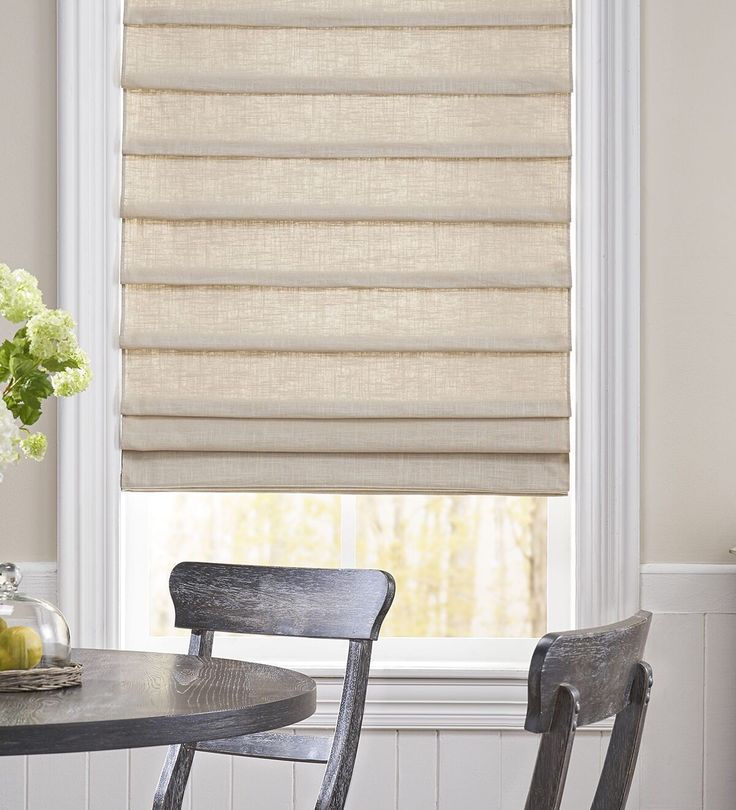 a dining room table with two chairs and a window covered in roman blind shades on the windowsill