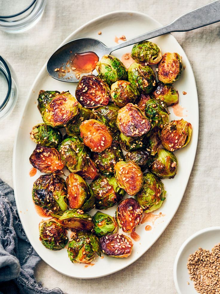 a white plate topped with brussel sprouts next to two bowls of seasoning