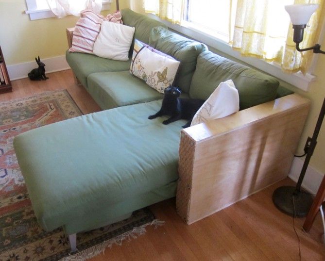 a cat sitting on top of a green couch in a living room next to a window