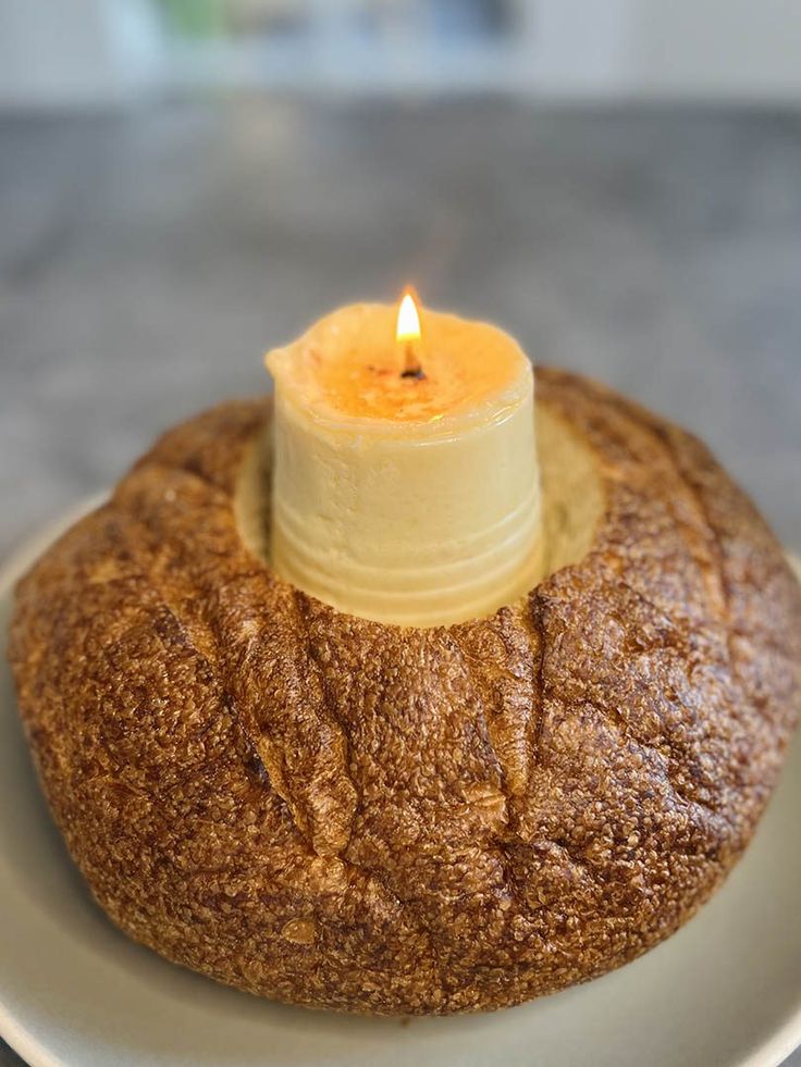 a candle is sitting on top of a round breaded bun that sits on a plate