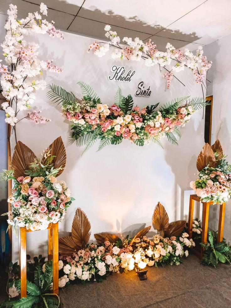 an arrangement of flowers and greenery in front of a white wall