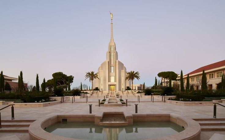 a fountain in front of a church with palm trees around it and stairs leading up to the building