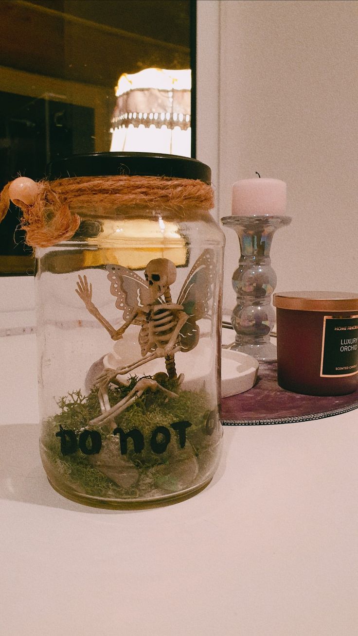 a glass jar with a skeleton inside sitting on a table next to candles and other items