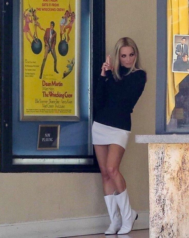 a woman standing in front of a movie poster holding her finger up to the camera