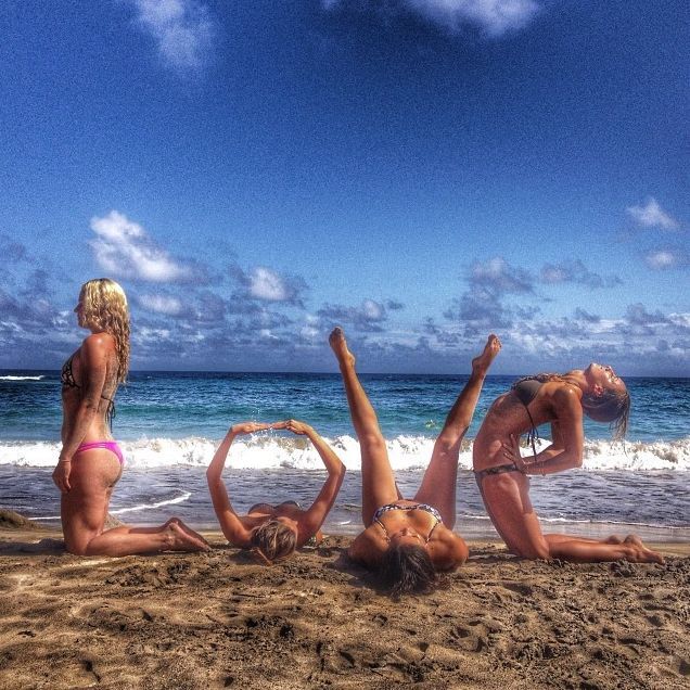 three women in bikinis doing yoga on the beach