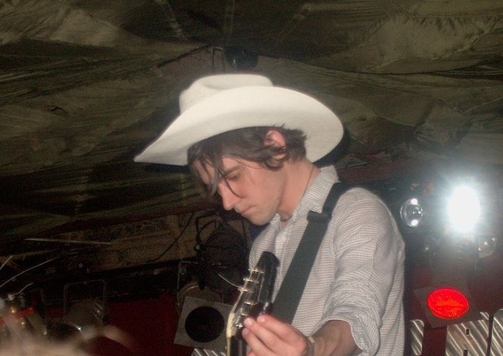 a man wearing a white cowboy hat and holding a microphone in his hand while standing under a tent