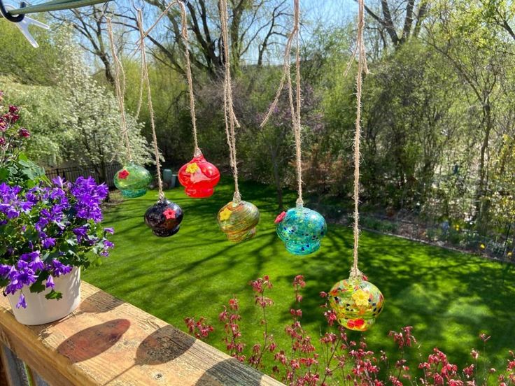 colorful glass balls hanging from the ceiling in a garden with purple flowers and green grass